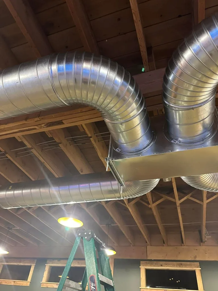 Commercial galvanized spiral duct manifold running along exposed rafters — clean, symmetrical Unlimited install