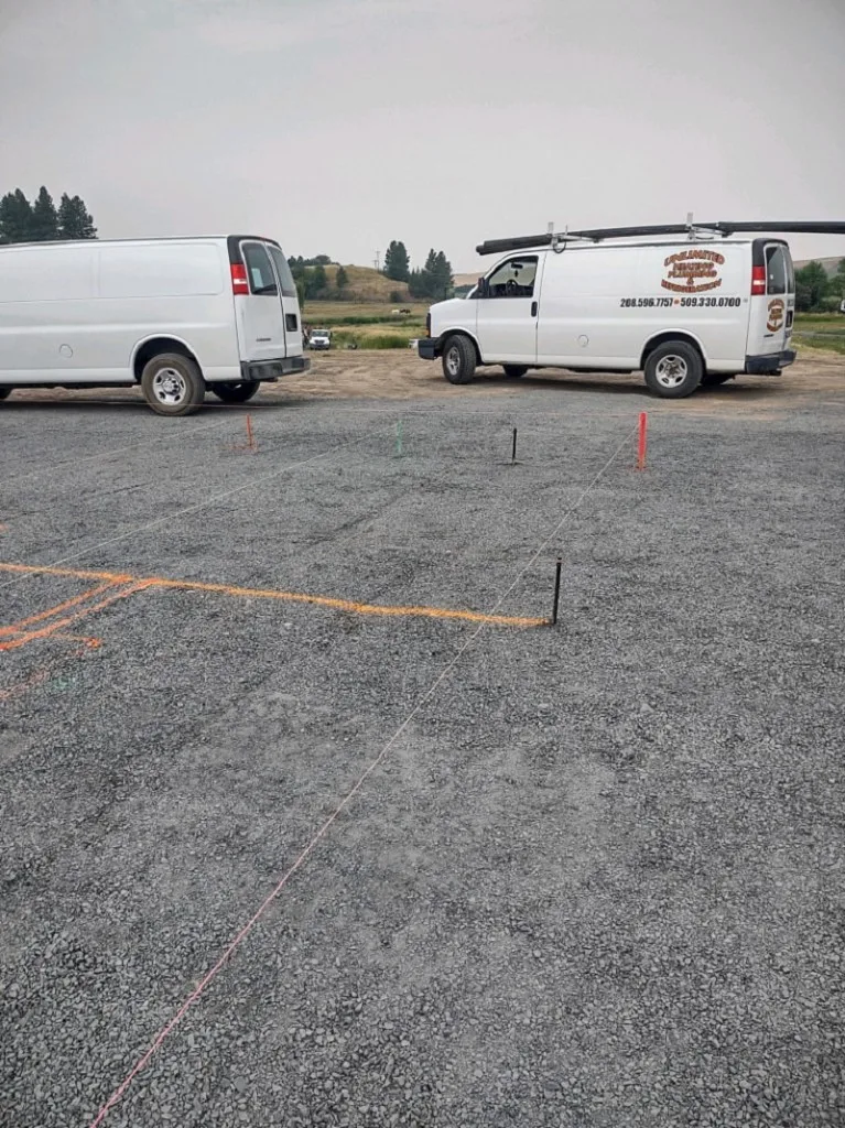 Two branded Unlimited Chevy Express vans on a gravel jobsite with survey stakes and layout strings for a new build