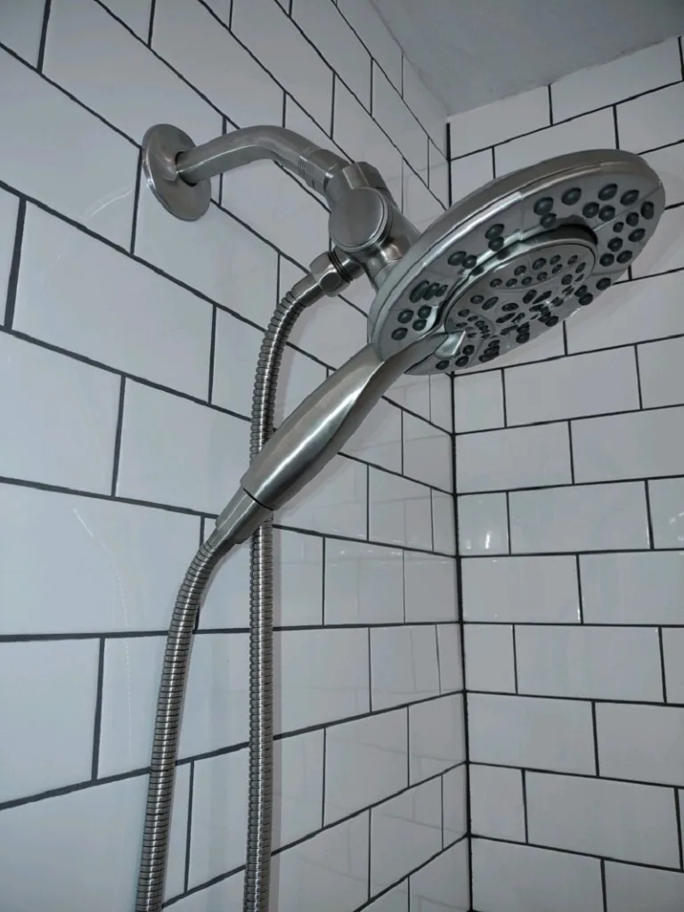 Modern brushed-nickel shower head and handheld wand on classic white subway tile with light grout