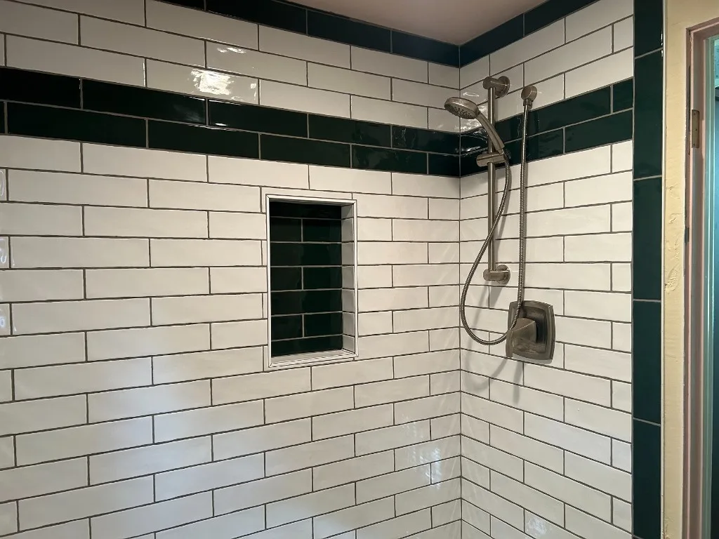 Premium subway-tile shower install with a dark green accent band, green tile niche, and brushed-nickel Moen fixtures on a handheld slide bar